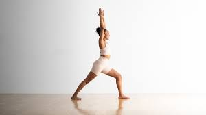 Woman practicing Virabhadrasana I (Warrior I Pose) yoga, standing in a lunge position with arms raised overhead.