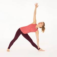 Woman practicing Trikonasana (Triangle Pose) yoga, stretching sideways with one hand on the floor and the other reaching upward.