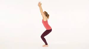 Woman practicing Utkatasana (Chair Pose) yoga, bending her knees and raising her arms overhead in a squat position.