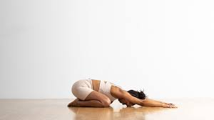 Woman practicing Balasana (Child's Pose) yoga, kneeling with her arms extended forward and forehead resting on the floor.