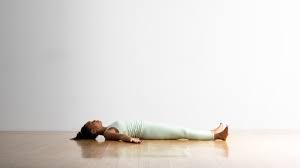 Woman practicing Savasana (Corpse Pose) yoga, lying flat on her back with arms relaxed by her sides.