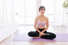 A Young Woman in a Pink Top and Black Leggings Sitting Cross-Legged on a Purple Yoga Mat.