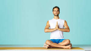 A Man in a White Sleeveless Shirt and Blue Shorts Sitting Cross-Legged on a Yoga Mat