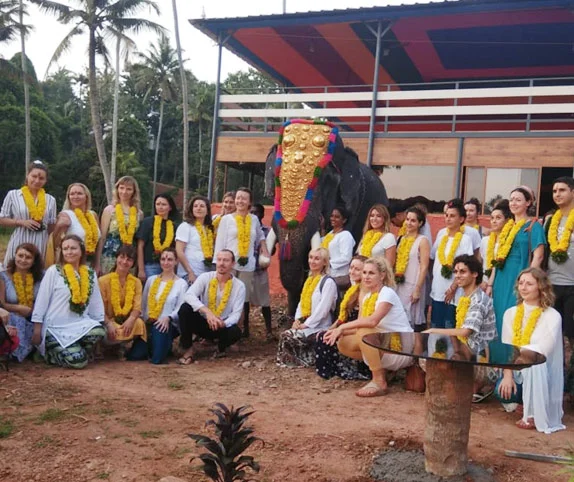 Group of yoga retreat participants posing with a decorated elephant