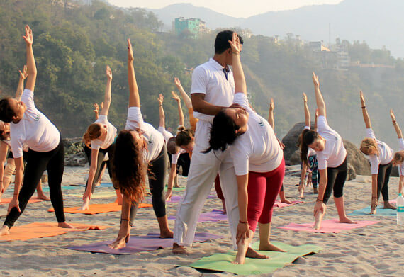 Yoga teacher assisting students in a beachside yoga class