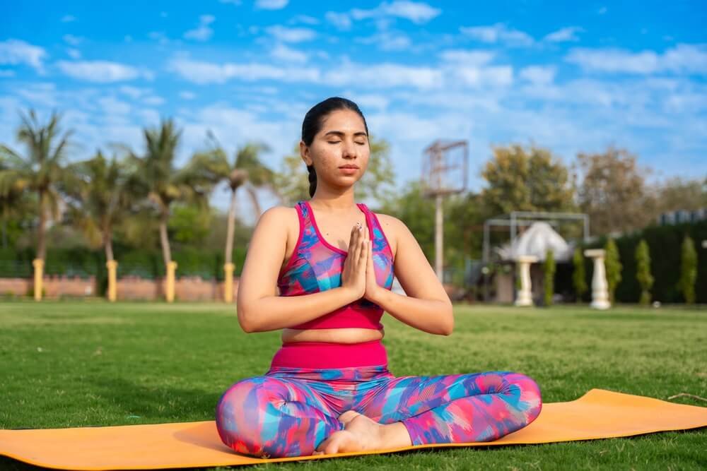 Young Woman Practicing Yoga Meditation Outdoors on a Mat, Enjoying Mindfulness and Relaxation in a Serene Natural Setting